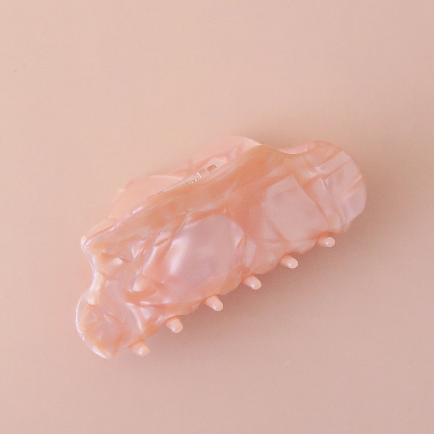 On a pink background is a light pink hair clip with a shell texture.