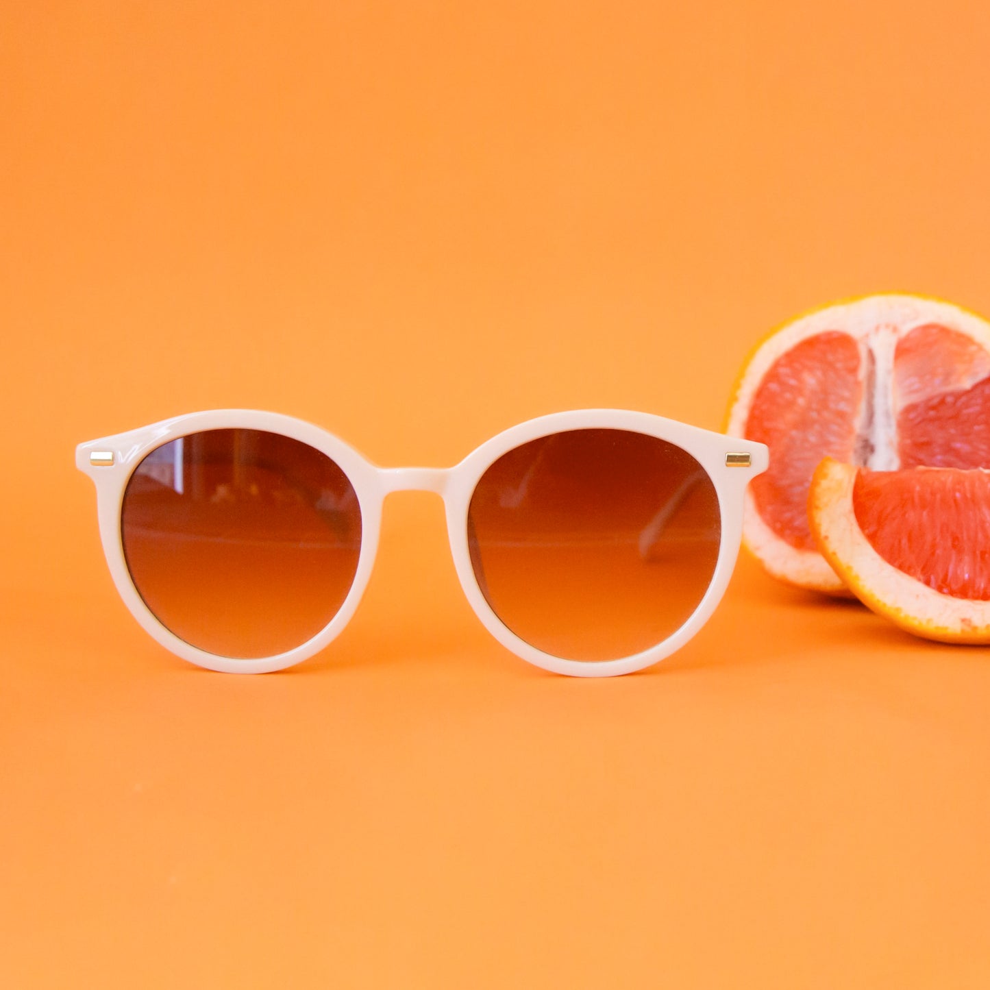 A white pair of rounded sunglasses with a brown lens.
