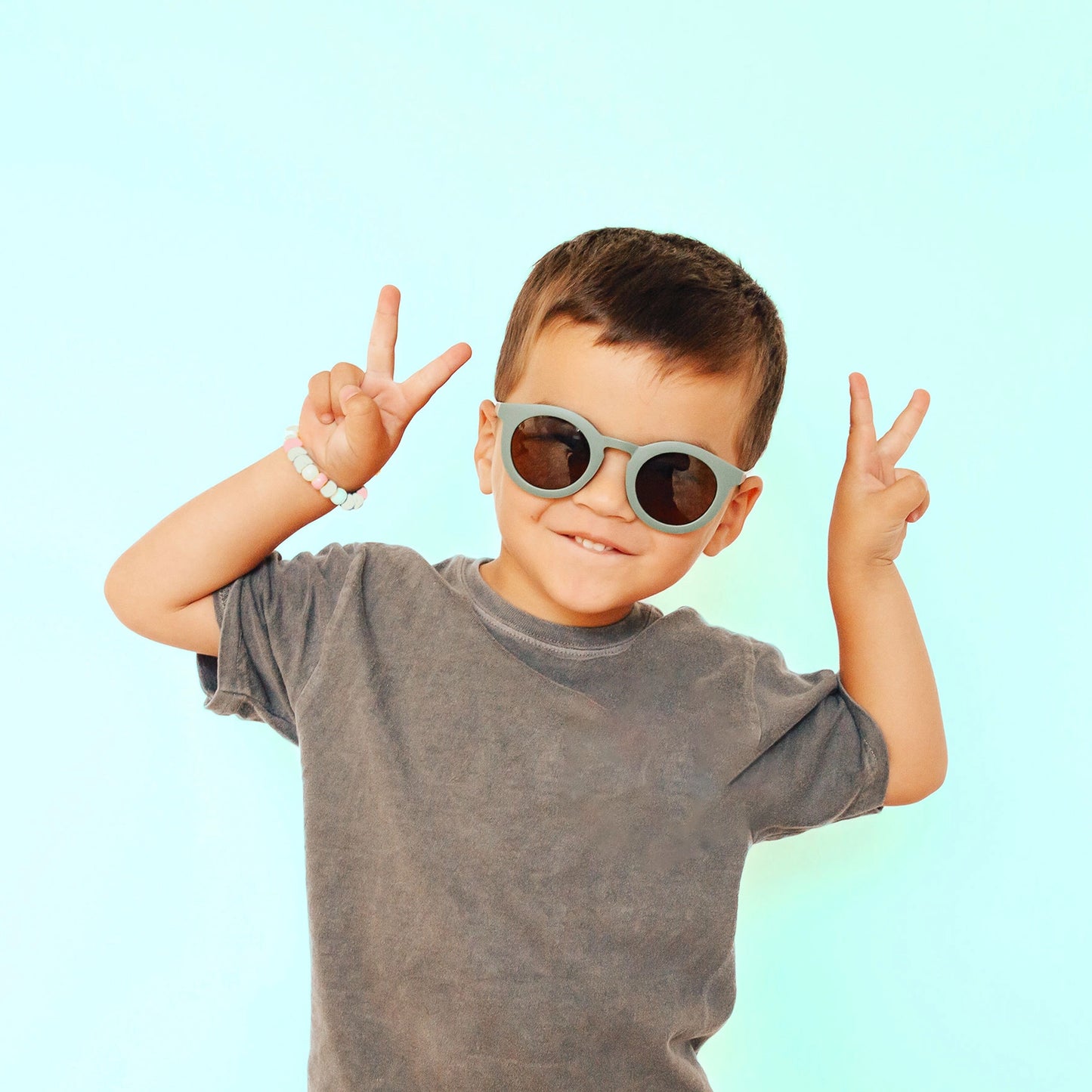 On a blue background is a model wearing a green pair of round shaped sunglasses.