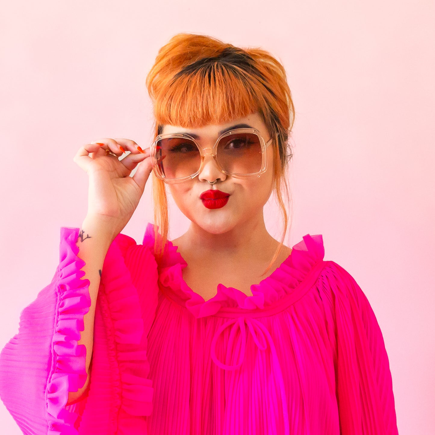 A pair of sunglasses with a clear peachy frame and pinkish gradient lenses.
