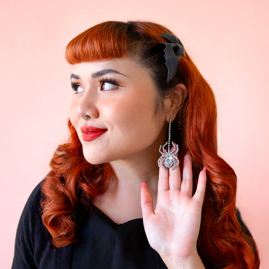 A red headed model wears a pair of sparkly spider shaped earrings.