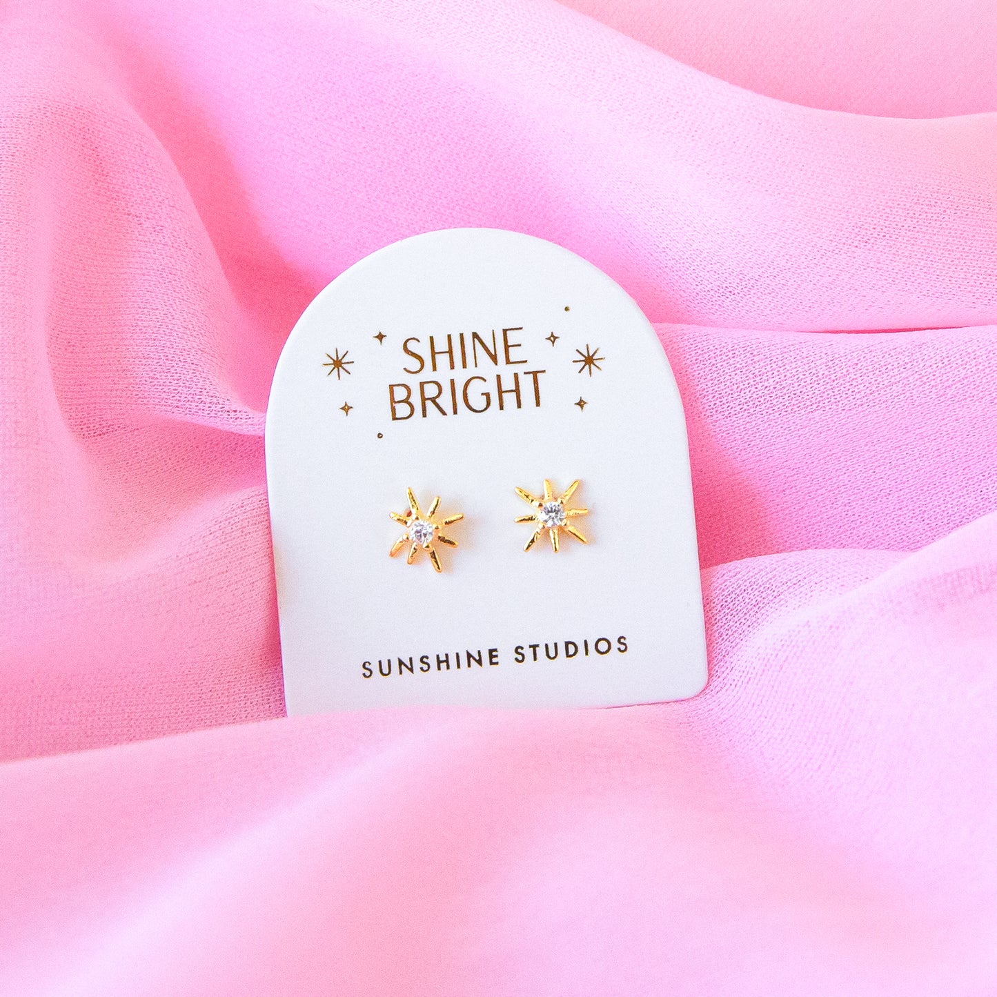 A pair of dainty gold star earrings with a CZ stone in the center.
