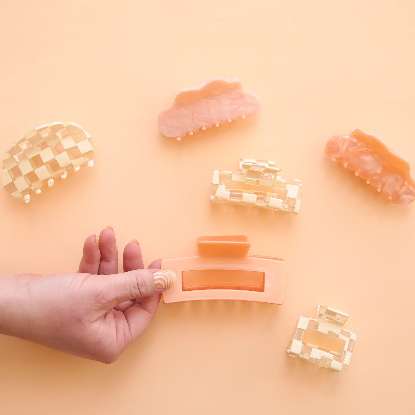 On a peachy background is a variety of different claw clips available on our site including checker patters and shades of pink.