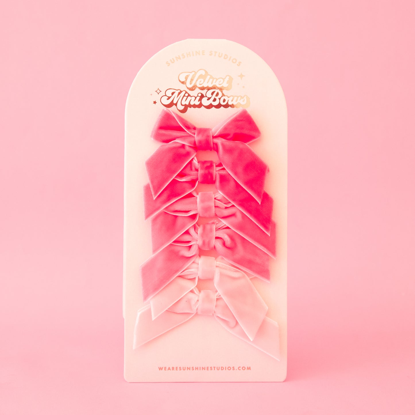 On a pink background is a velvet set of six mini bows in different shades of pink.