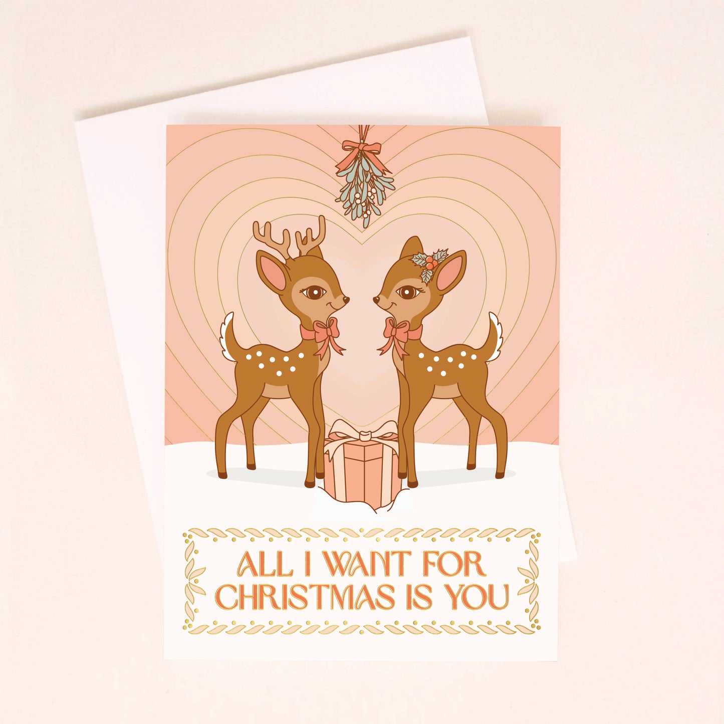On a neutral background is a light pink card with two brown retro deer looking towards one another underneath mistletoe with a gradient heart in the background and text below the image that reads, "All I Want For Christmas Is You".
