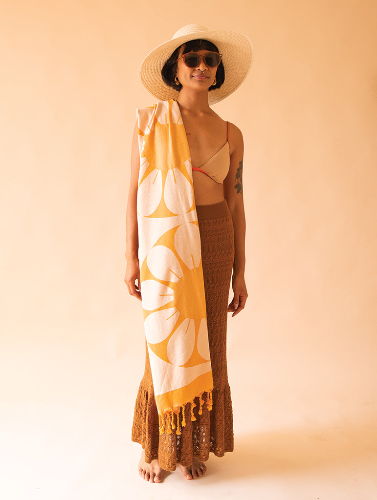 a woman wearing a straw hat and sunglasses wears a yellow towel with large white flowers over her shoulder