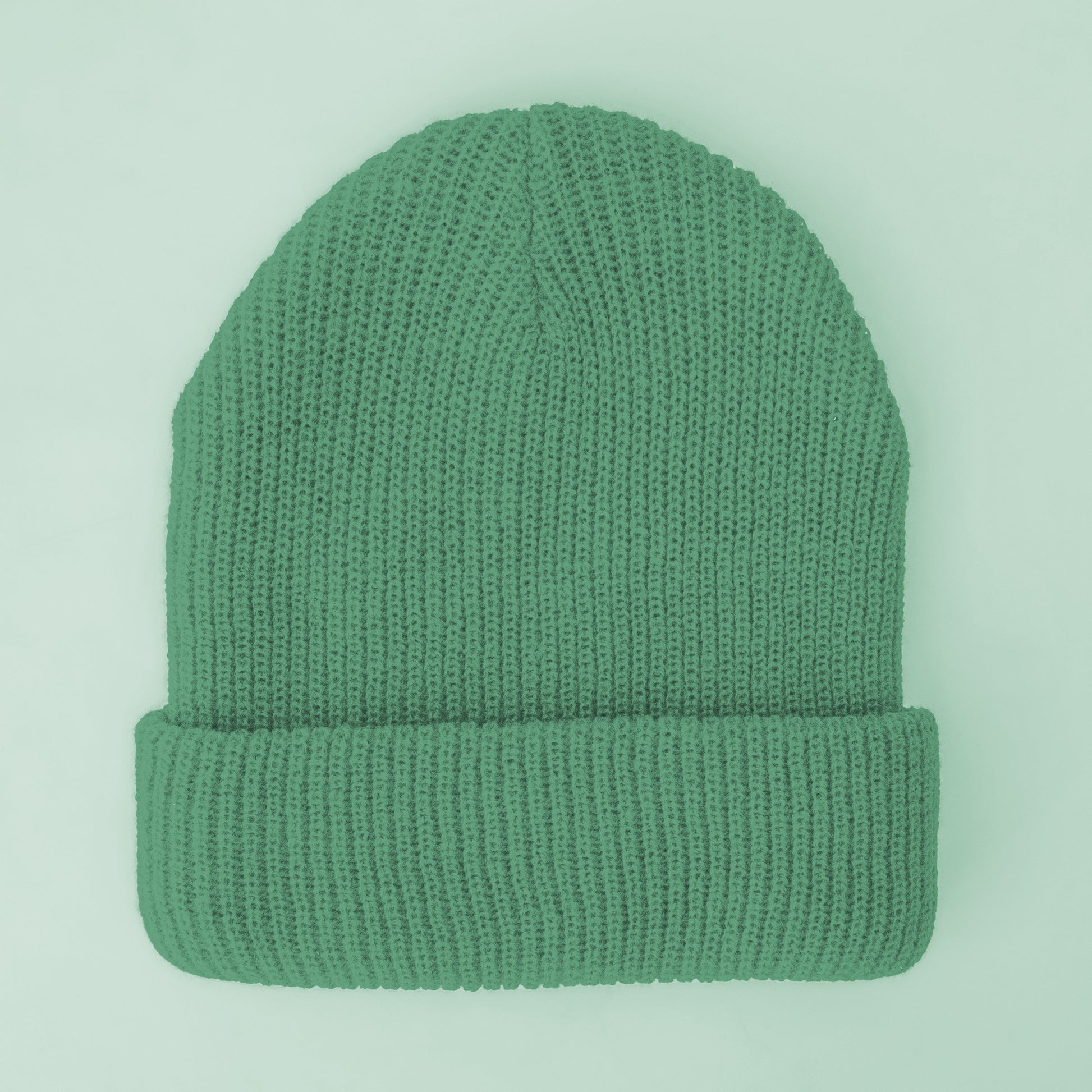 A jade colored knit beanie sits on a mint green ground.