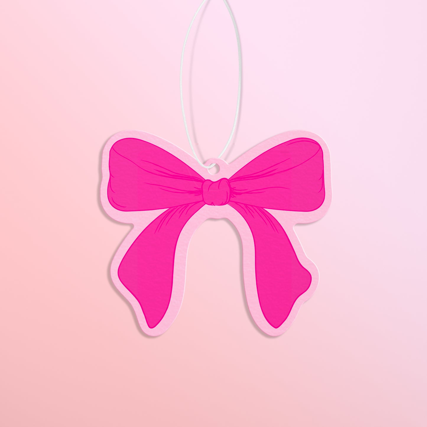 Hot pink bow with light pink trim air freshener is shown against a light pink to peach gradient background