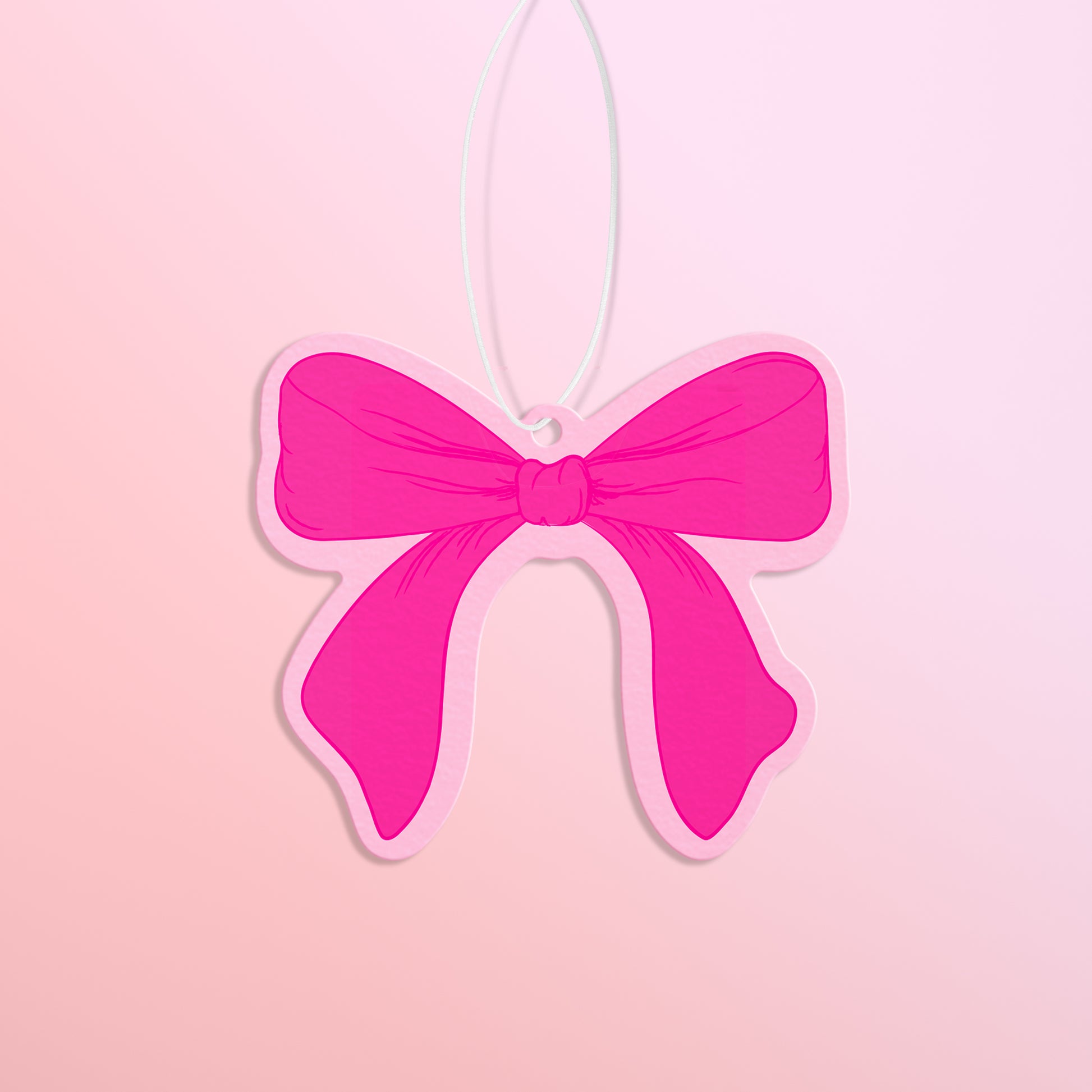 Hot pink bow with light pink trim air freshener is shown against a light pink to peach gradient background