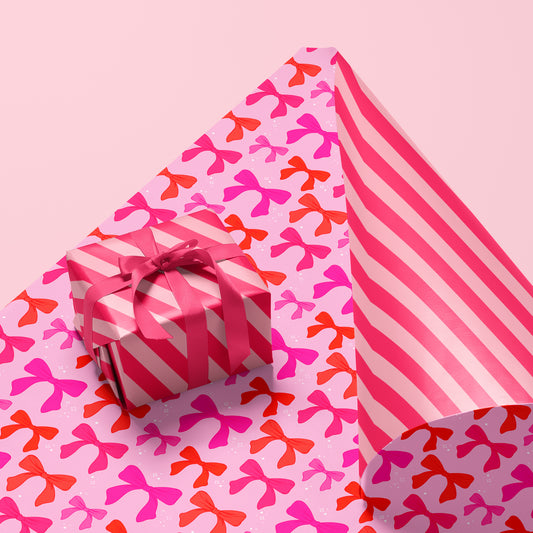 A pink and red piece of wrapping paper with a reversible pattern. One side features a bow pattern and the other, a pink stripe. Box and bow not included with purchase.