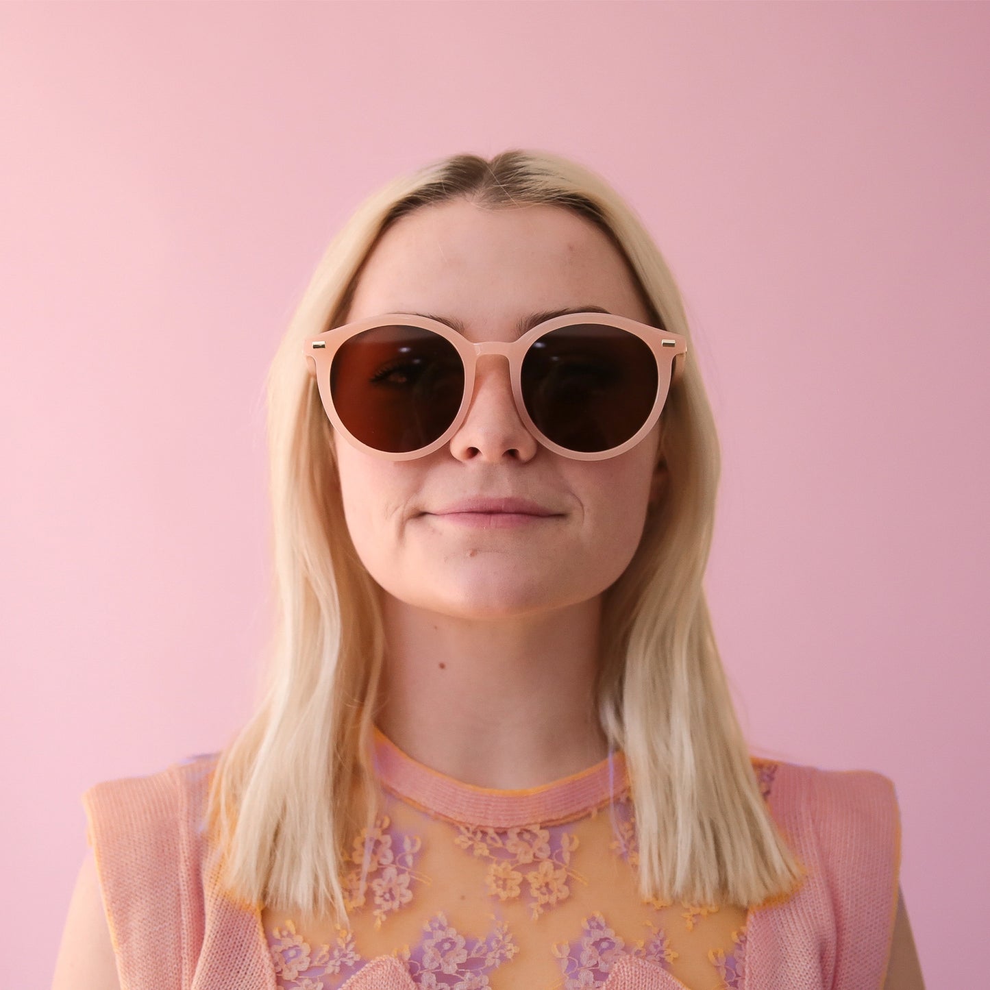 On a pink background is a model wearing the Sam sunglasses in pink.