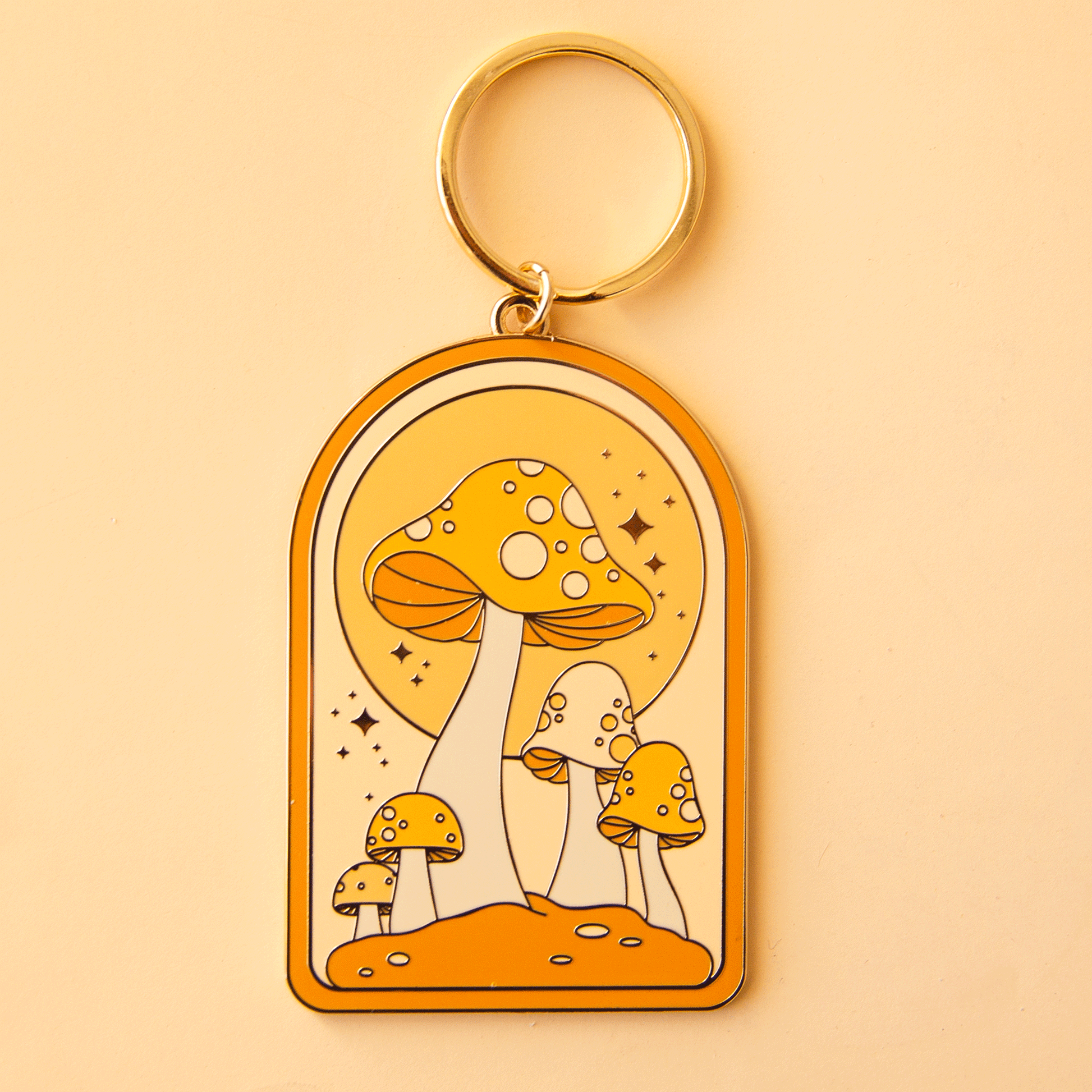 On a yellow background is an arched metal keychain is a gold loop and a mushroom design.