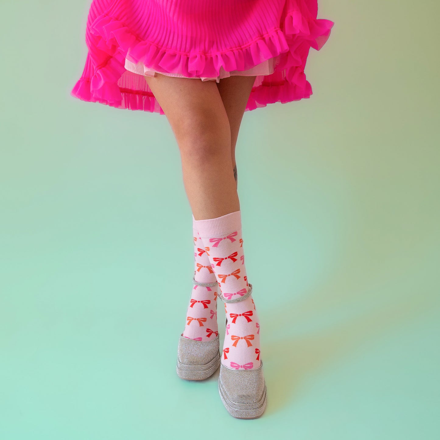 A pair of light pink socks with red, orange and pink bow patterns all over. 