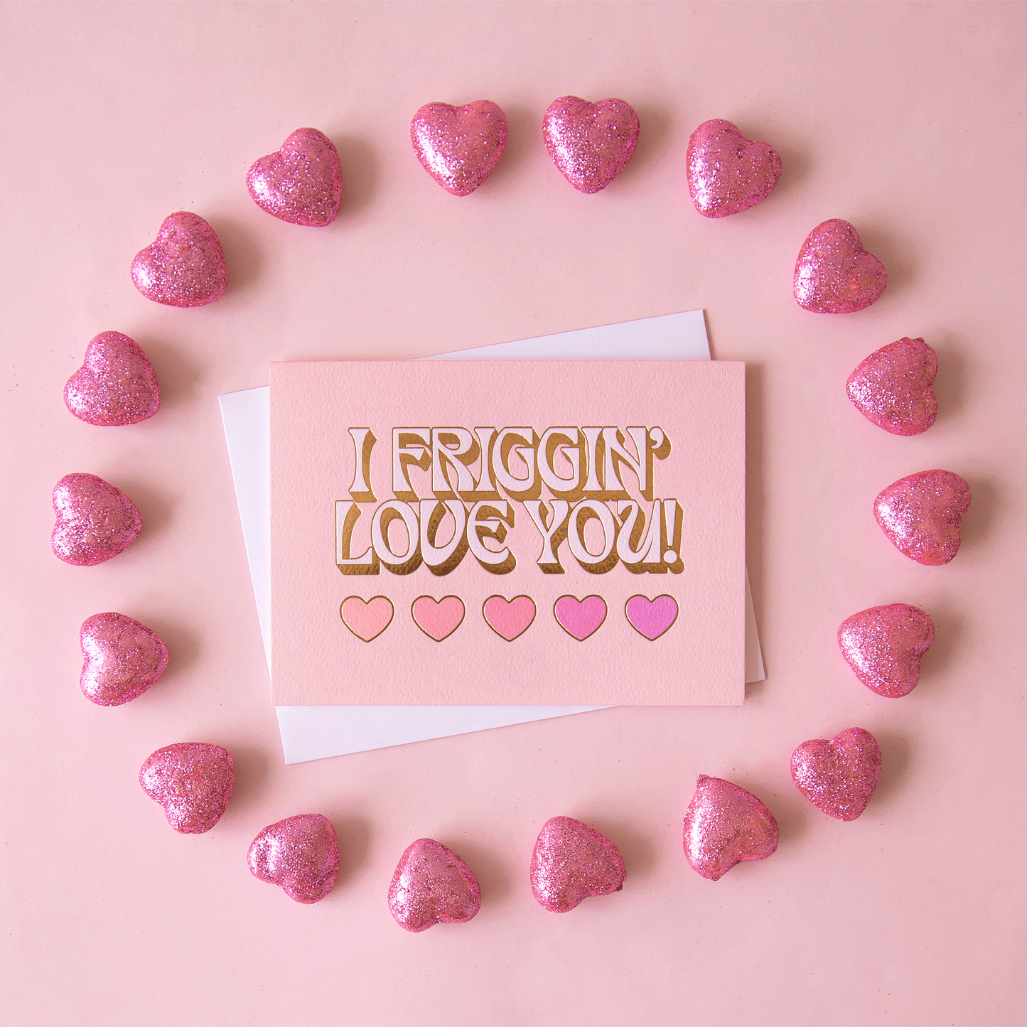 On a pink background is a light pink card with text that reads, "I Friggin' Love You!" with five hearts underneath.