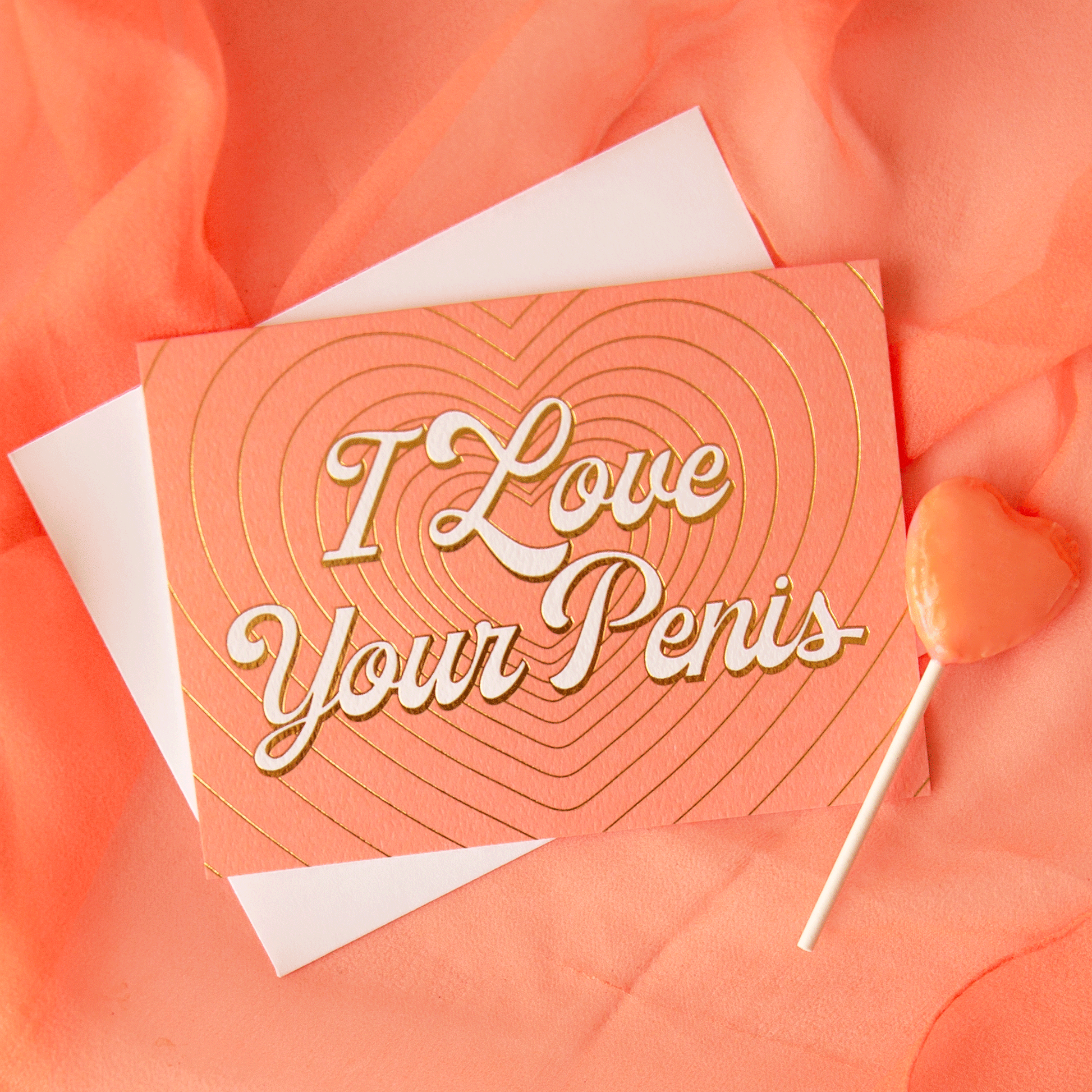 On a peachy background is a peachy colored card with layered gold foiled hearts and ivory text that reads, "I Love Your Penis" along with a white envelope.On a peachy background is a peachy colored card with layered gold foiled hearts and ivory text that reads, "I Love Your Penis" along with a white envelope.