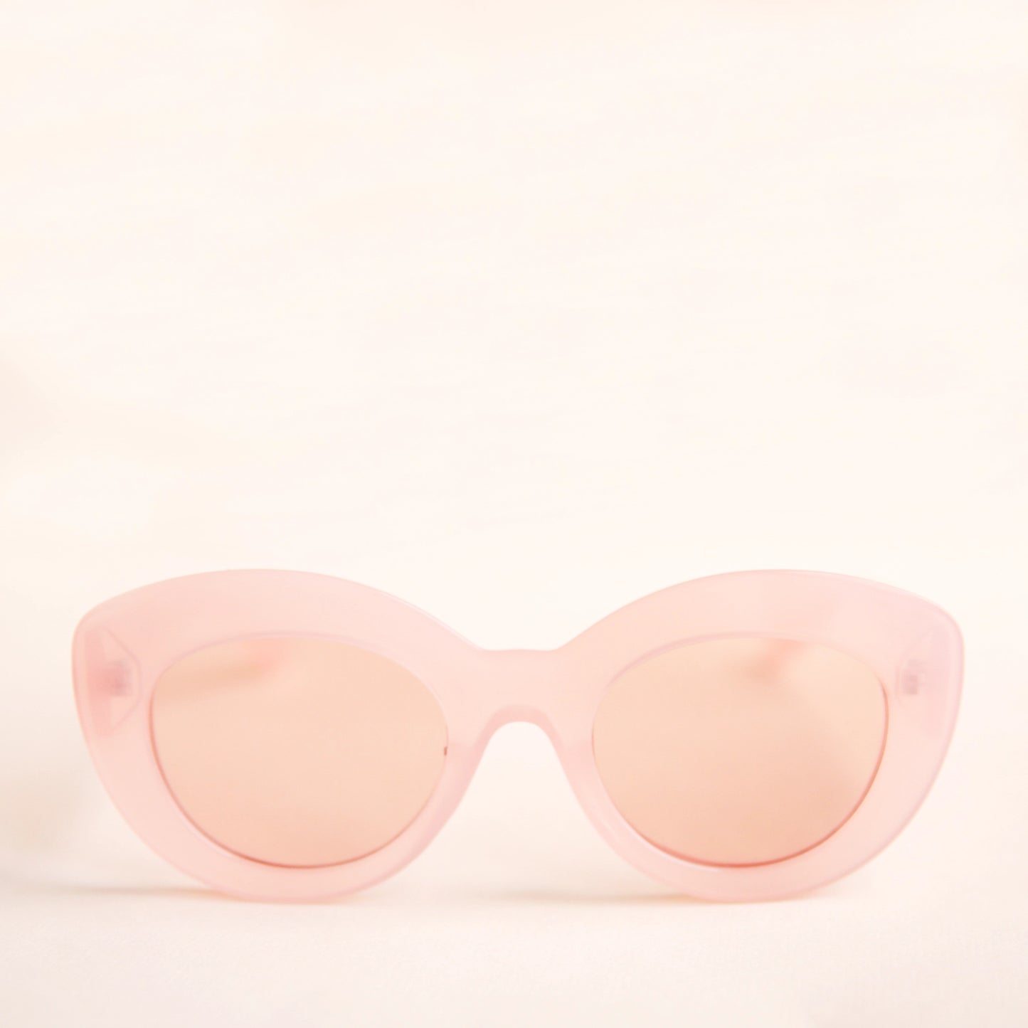 On a neutral background is the Gemma Sunglasses in a light pink shade. They have a rounded shape with a slight cateye flair at the corners. The frame material is a durable plastic and the lenses are a similar tone.