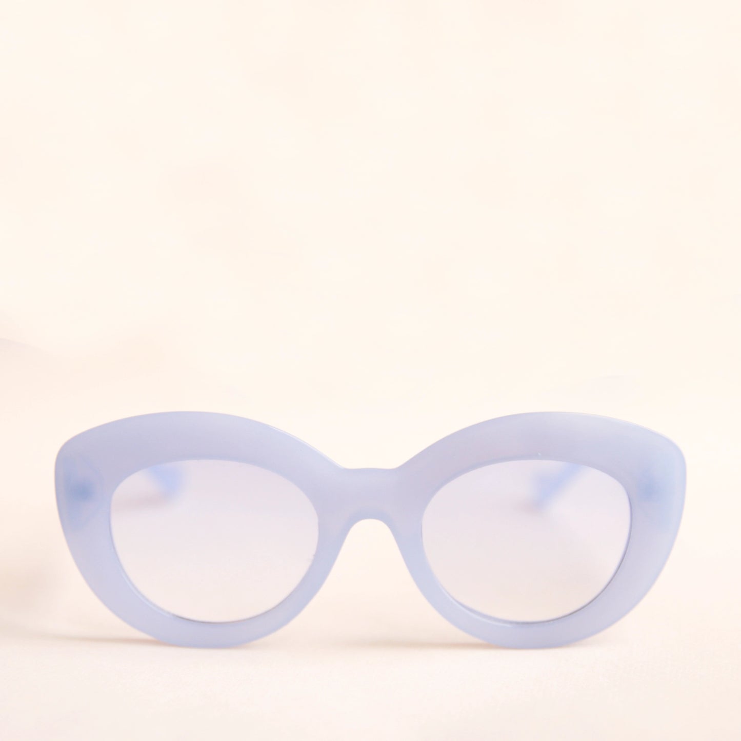 On a neutral background is the Gemma Sunglasses in a light blue shade. They have a rounded shape with a slight cateye flair at the corners. The frame material is a durable plastic and the lenses are a similar tone.