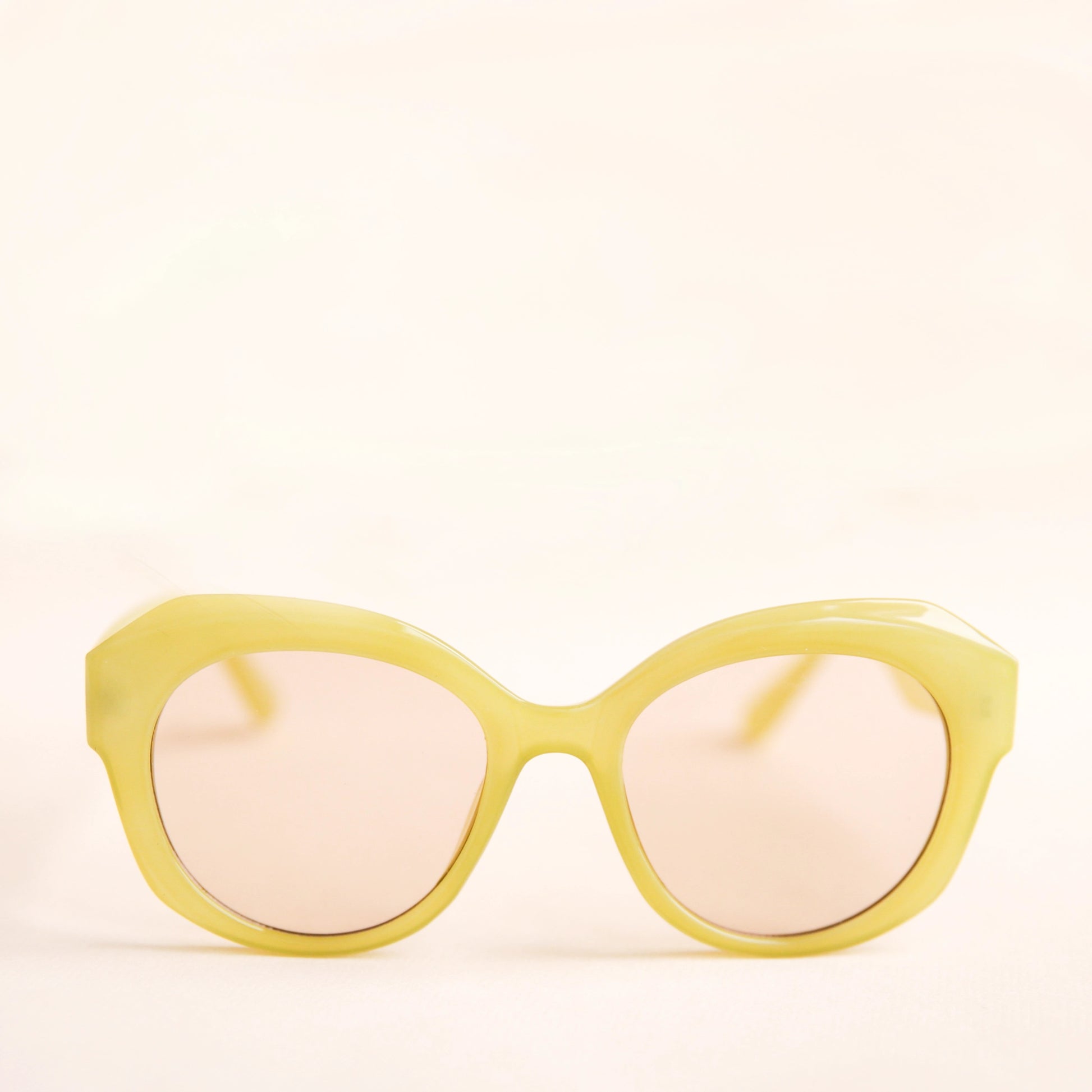 On a white background is a round pair of light green sunglasses with a light brown lens.