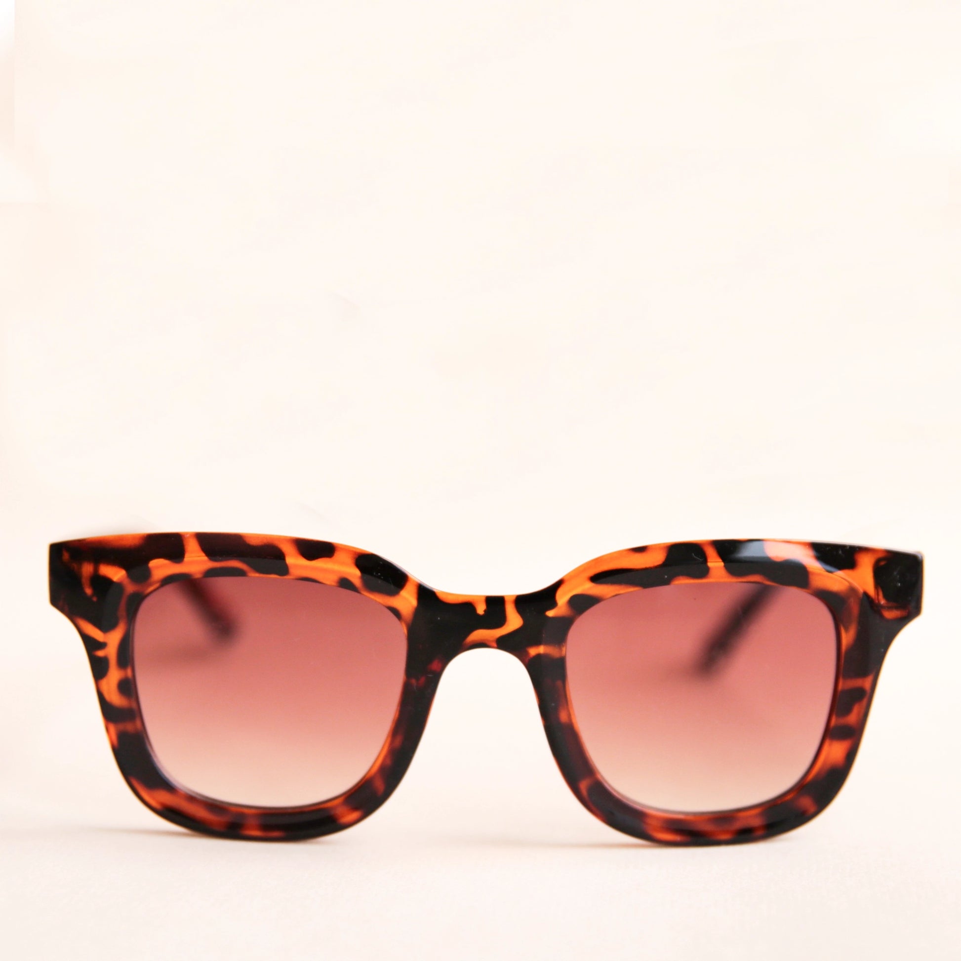 On a white background is a square pair of sunglasses with a brown and black tortoise pattern and a light brown lens.