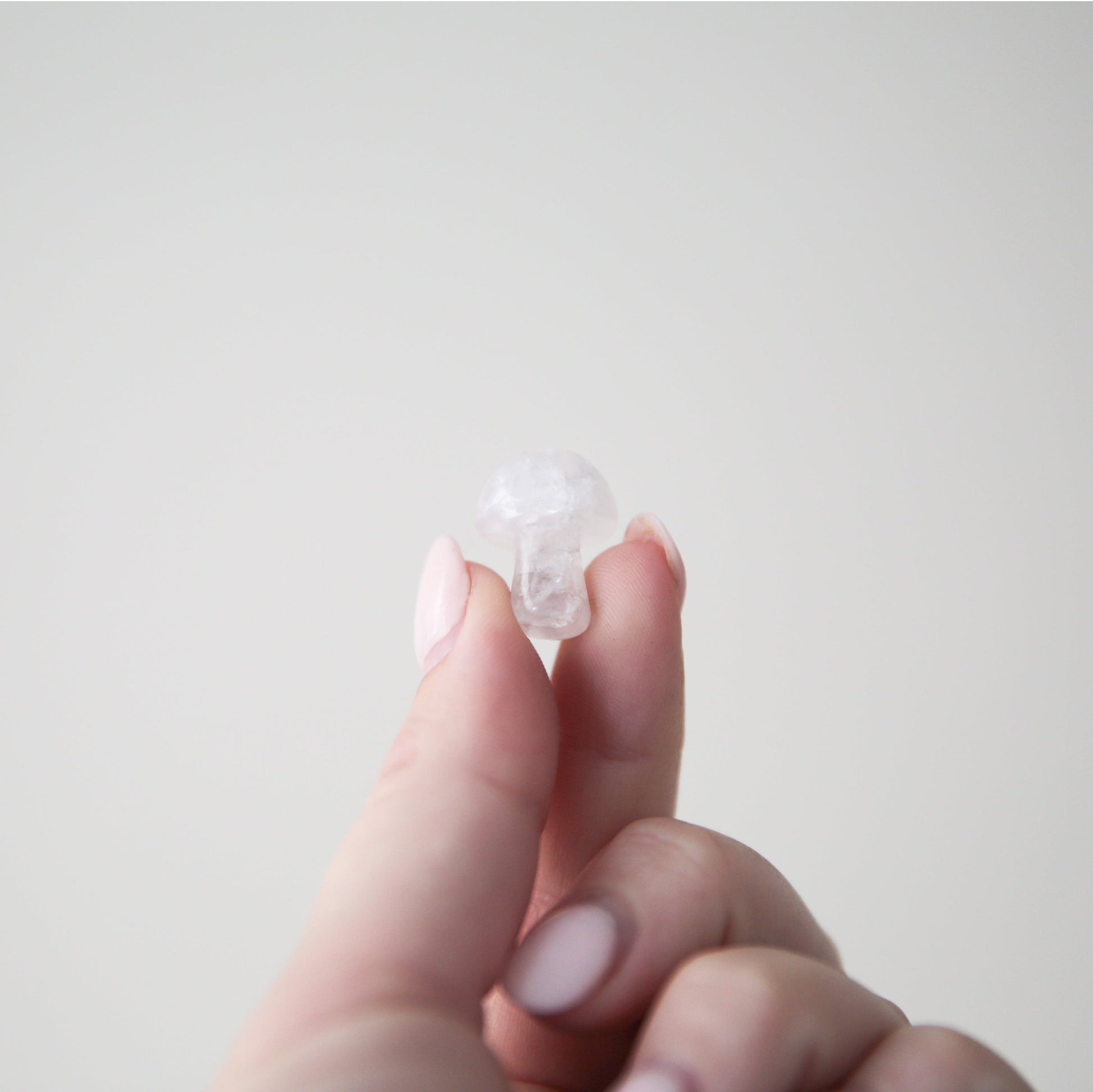 On a light grey background is a model holding a white quartz crystals in the shape of a tiny mushroom.