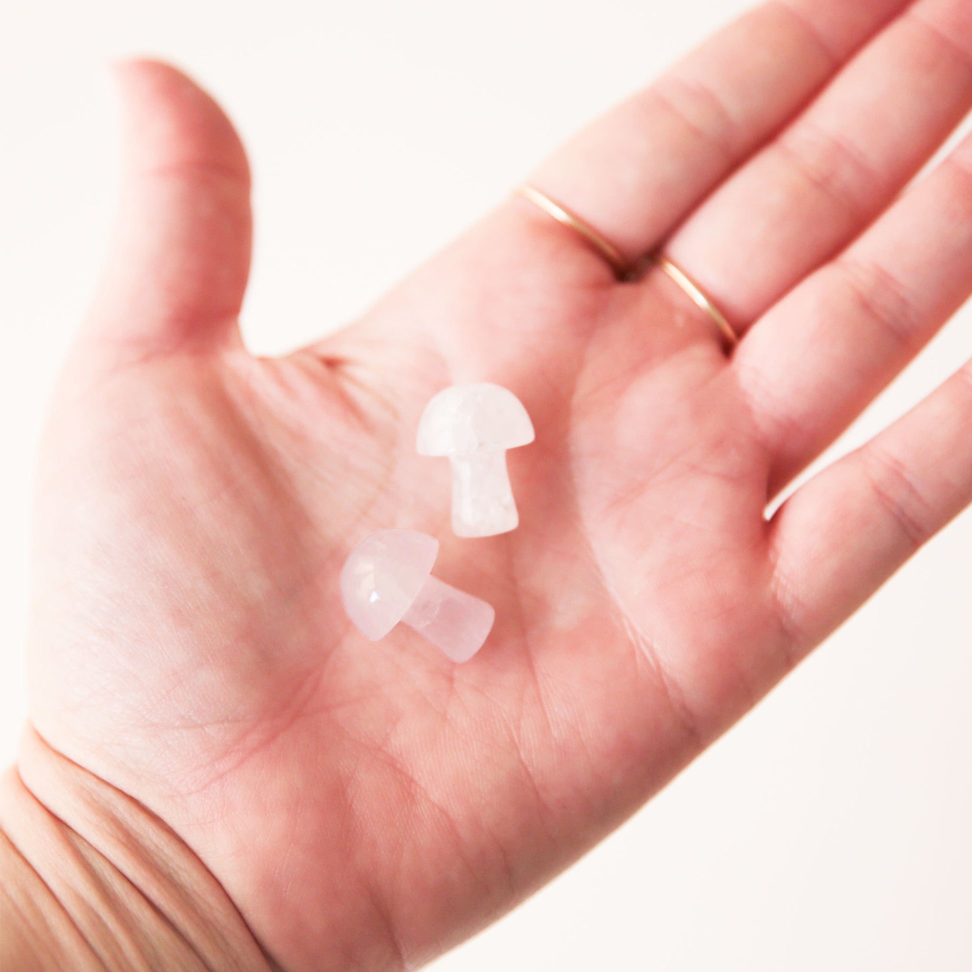 On a light grey background is a model holding two white quartz crystals in the shape of tiny mushrooms. 