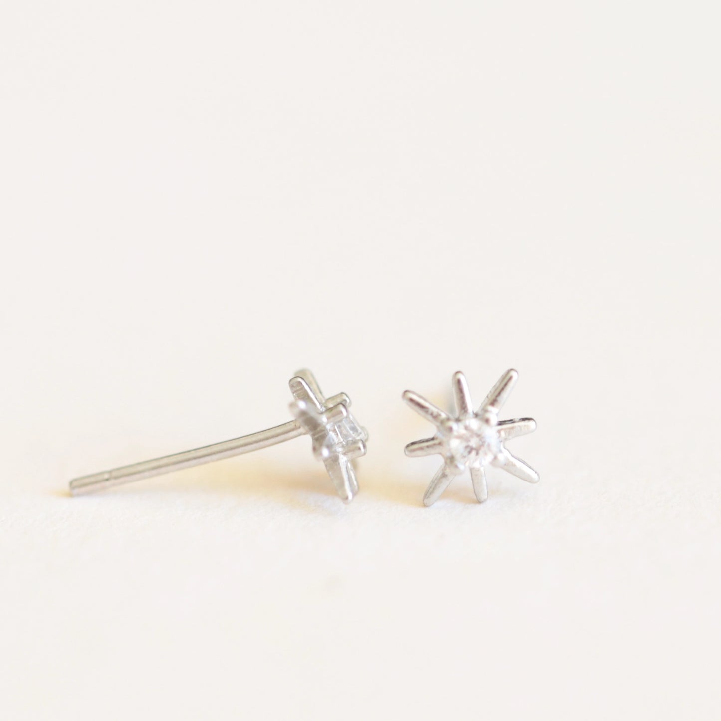On an ivory background is a pair of dainty silver star earrings with a CZ stone in the center.