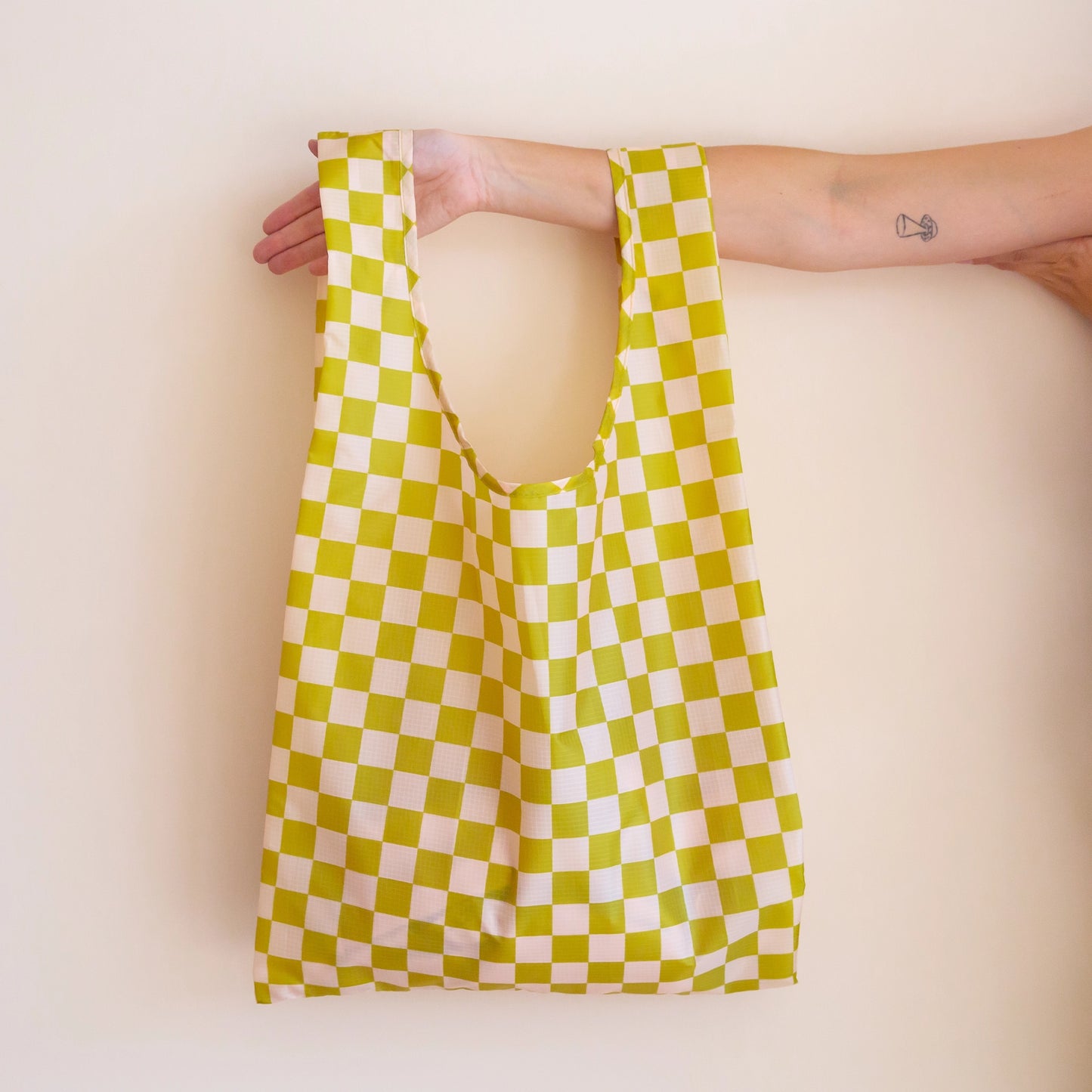 On a light pink background is light green and ivory checkered reusable nylon bag. 