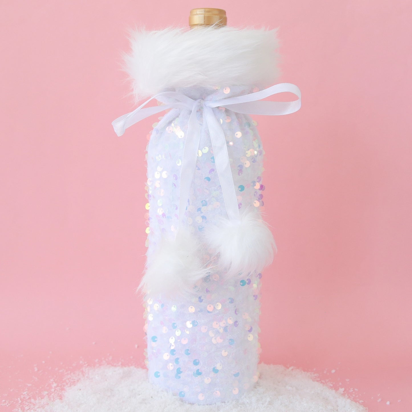 On a pink background is a iridescent and white wine bag with fluffy white faux fur lining the top and a pom pom bow to tie.