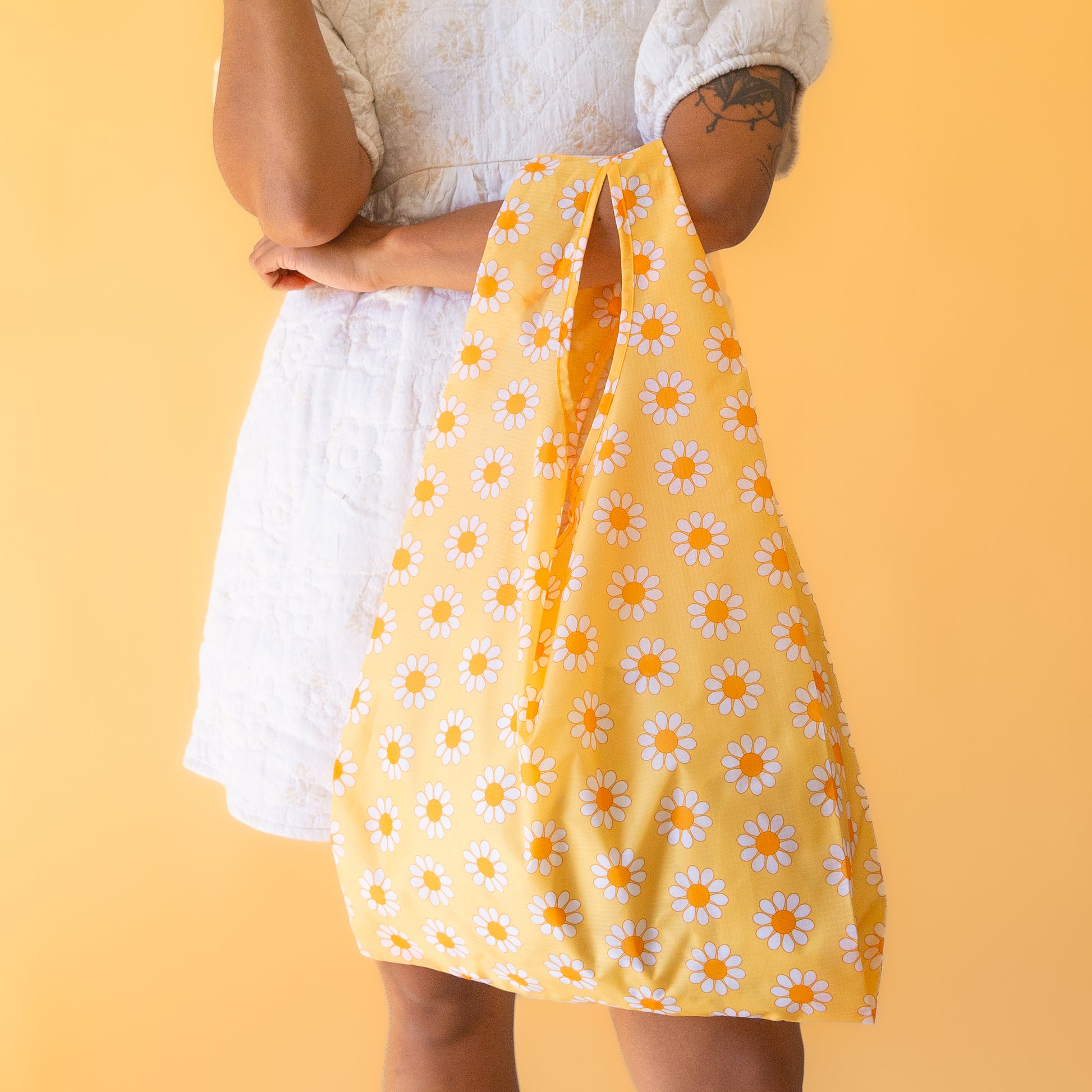 On a yellow background is a yellow, orange and white daisy pattern nylon bag.