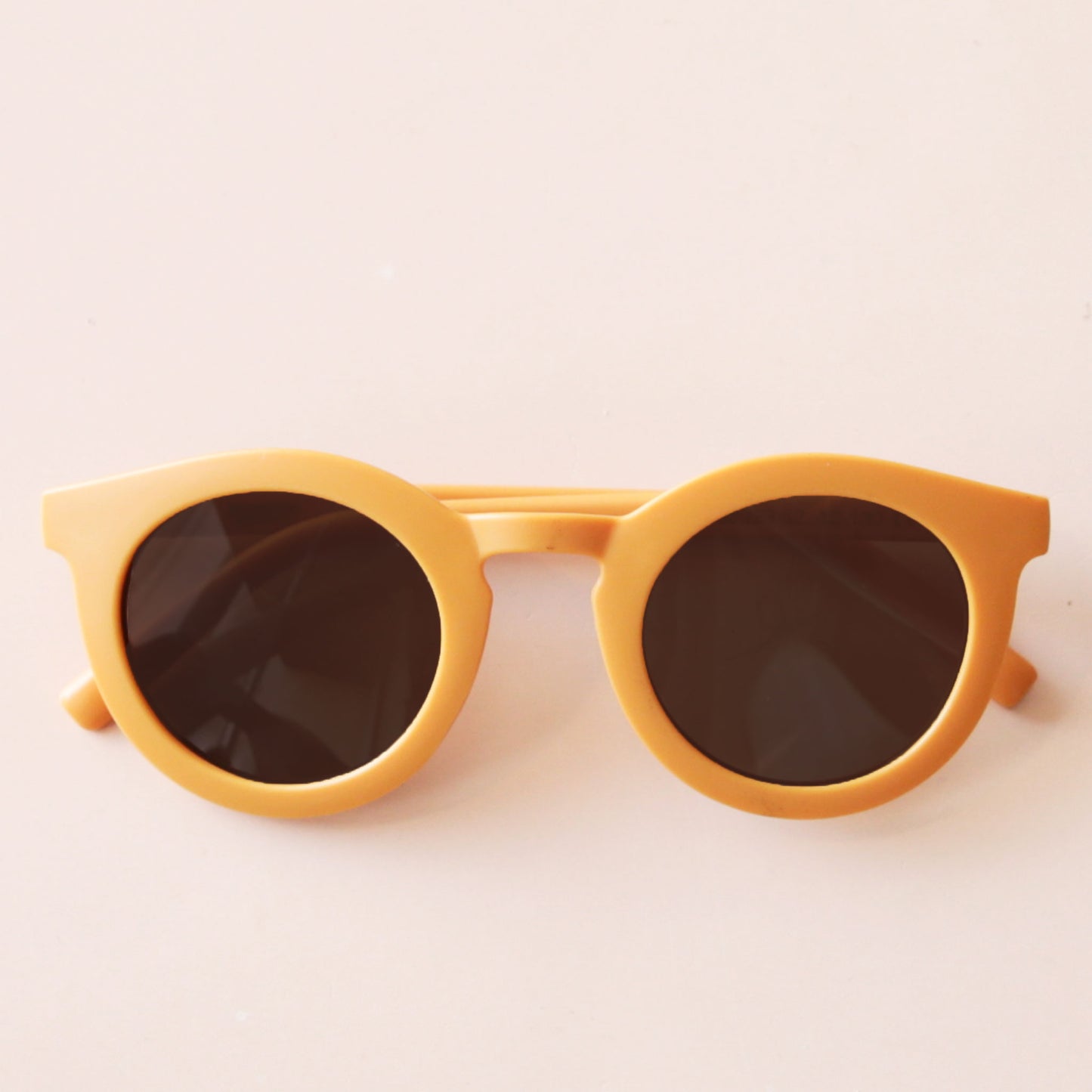 On a neutral background is a yellow pair of circle children's sunglasses.
