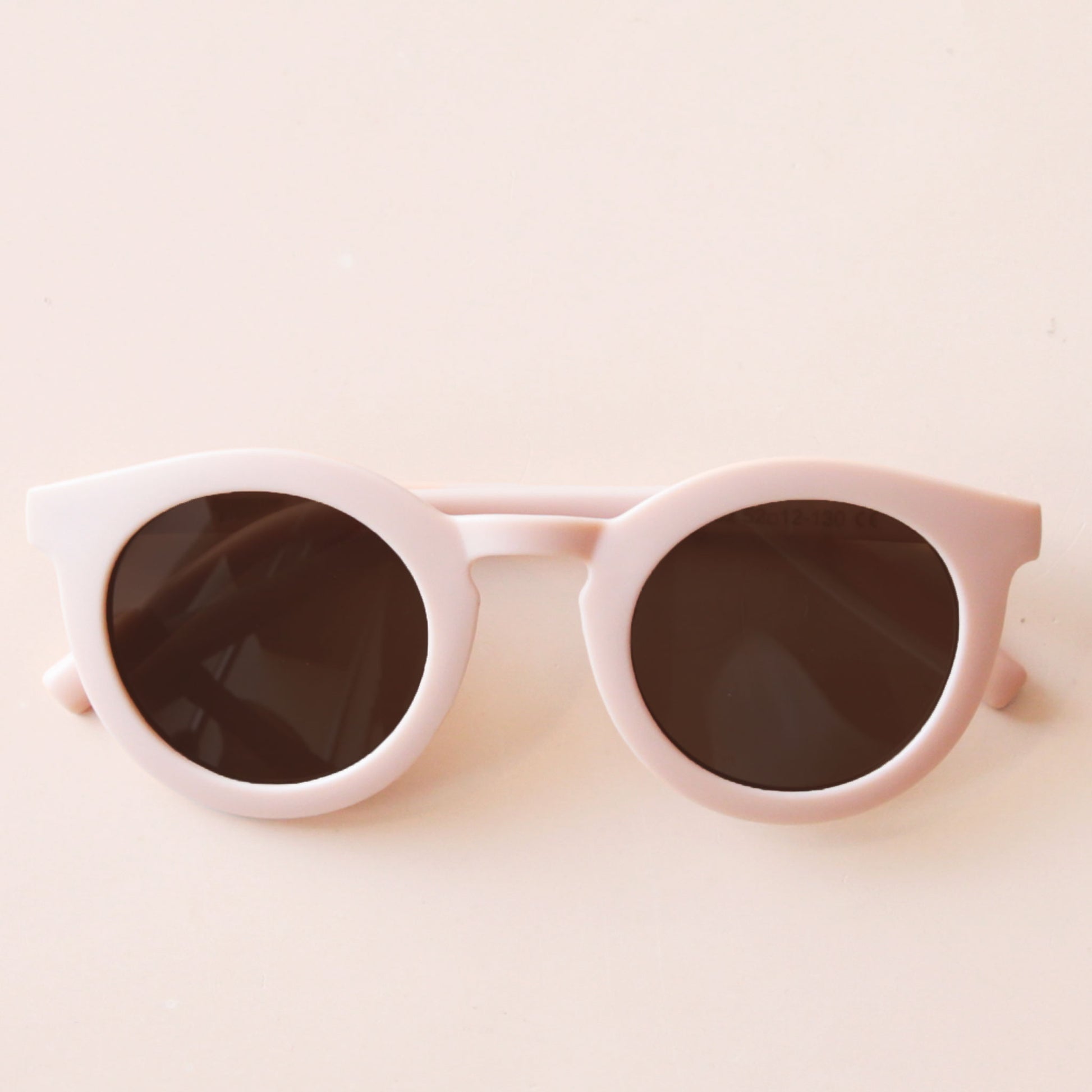 On a neutral background is a light pink children's sunglass with a round shape.
