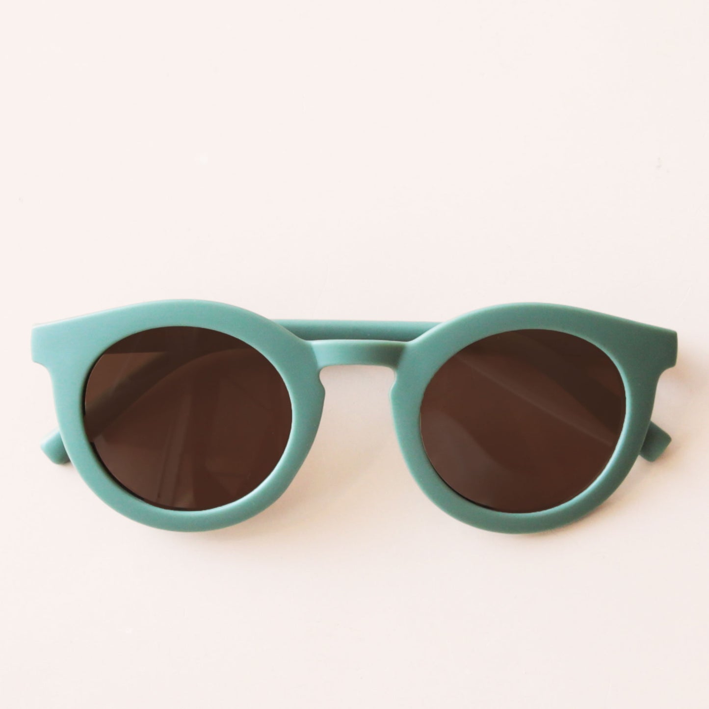 On a neutral background is a green pair of circle shape children's sunglasses.