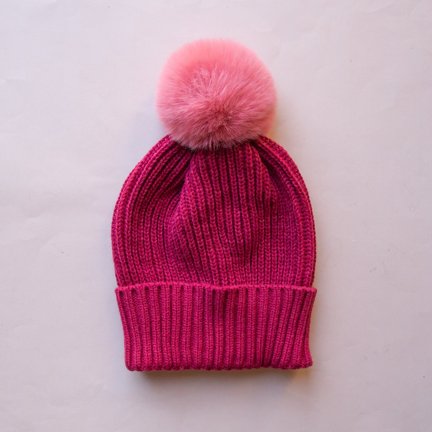 A dark pink beanie with a lighter pink pom at the top. 