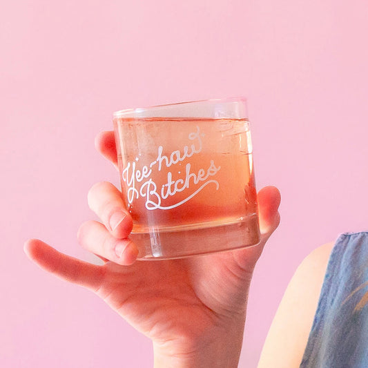 A short glass tumbler with white screenprinted text that reads, "Yee-haw Bitches".