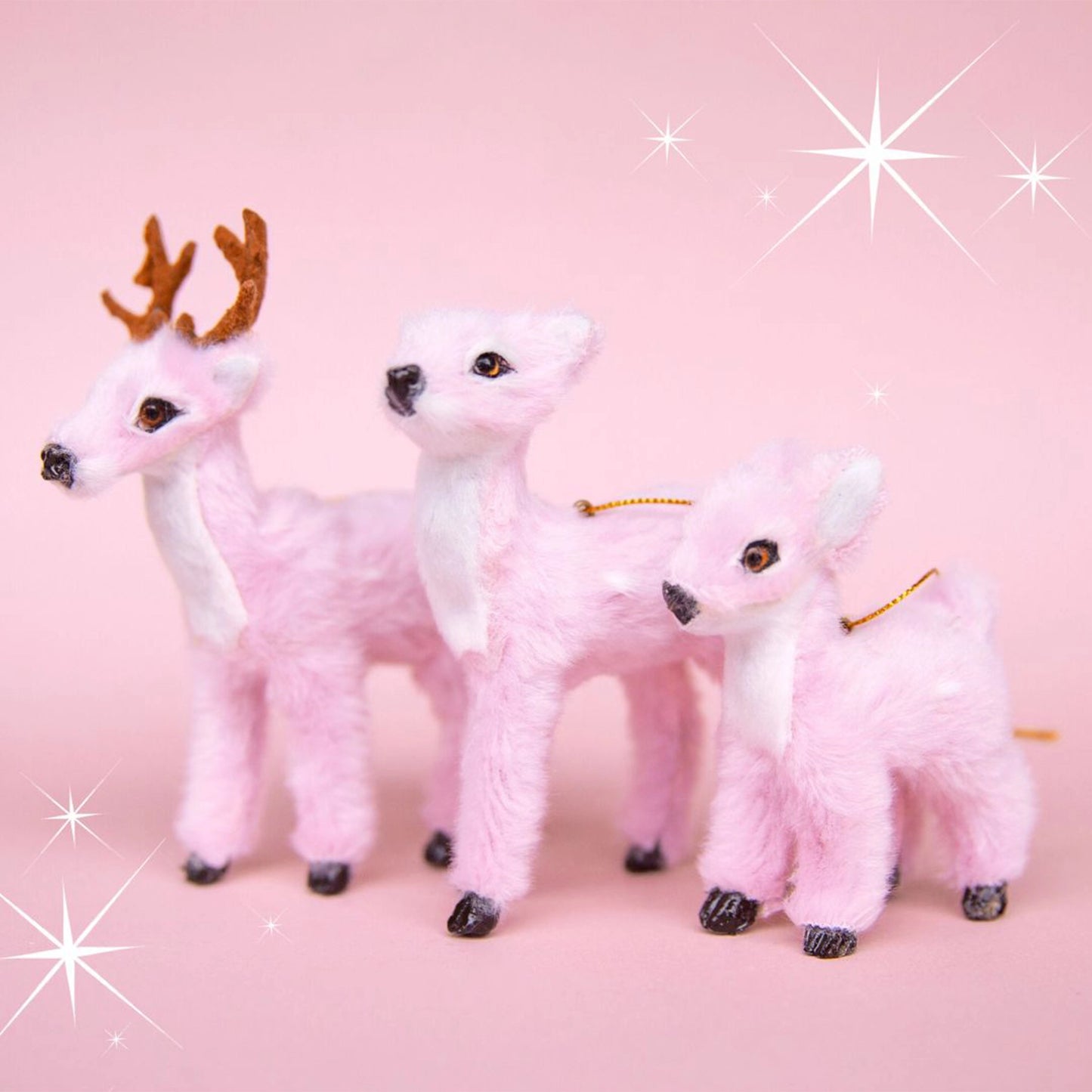 On a pink background is three fur reindeer ornament. 