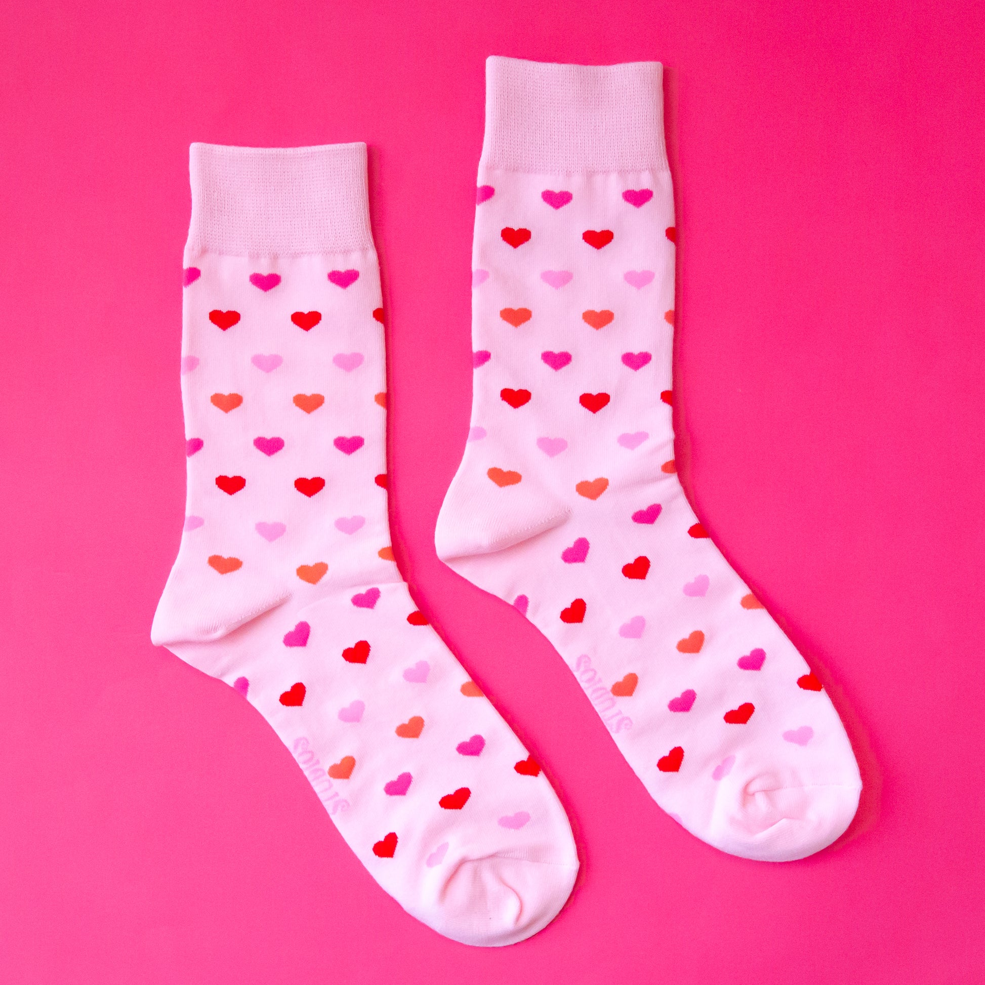 A  pair of crew socks with a heart print that is in different shades of pink. 