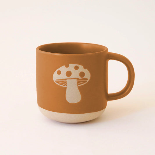 On an ivory background is a ceramic mug with a light colored mushroom design. 