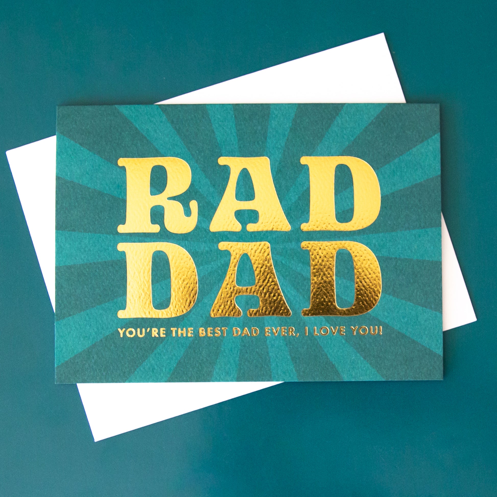 On a green background is a blue teal card with gold text that reads, "Rad Dad You're The Best Dad Ever, I Love You".