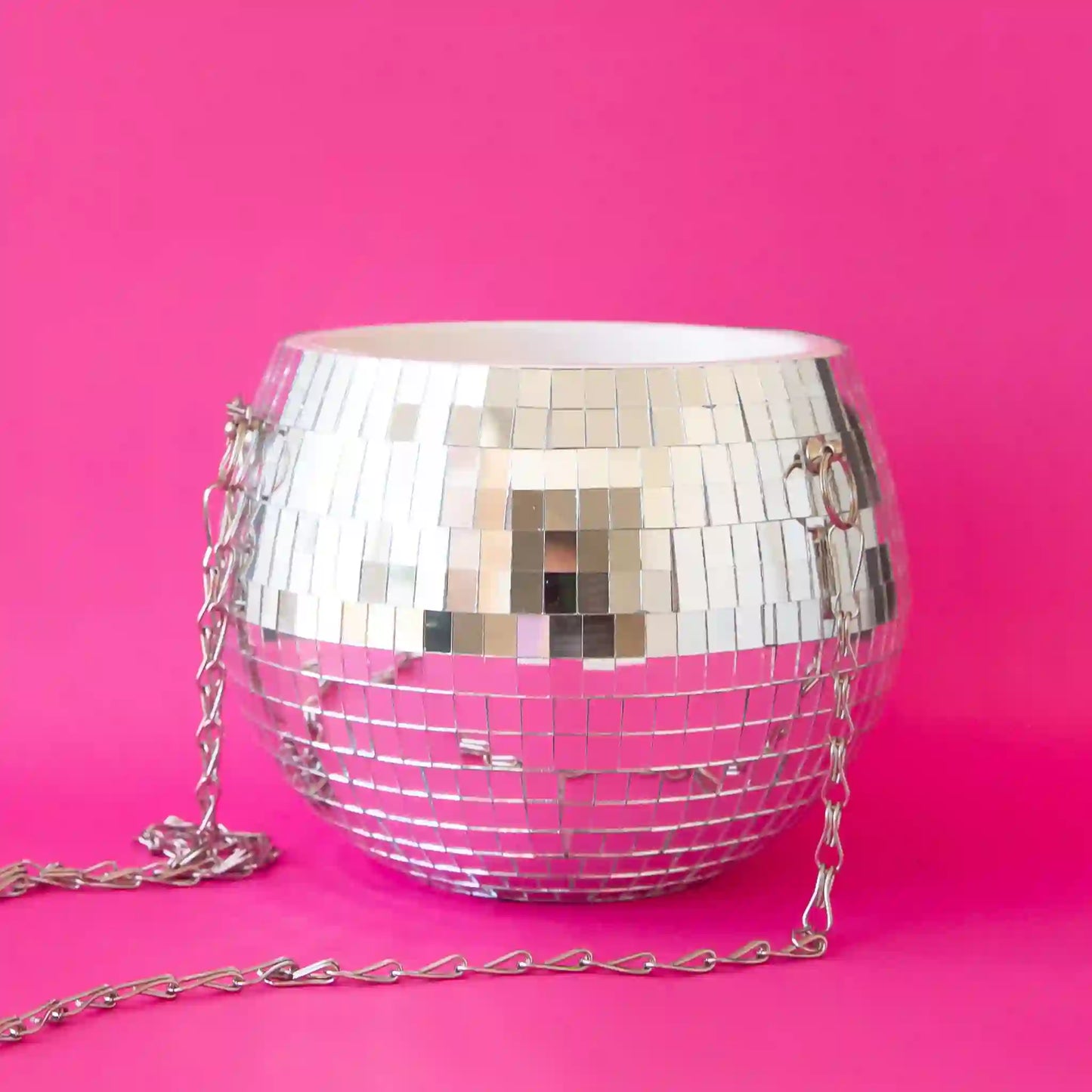 On a hot pink background is a silver mirrored glass disco ball shaped planter with a silver chain hanger.