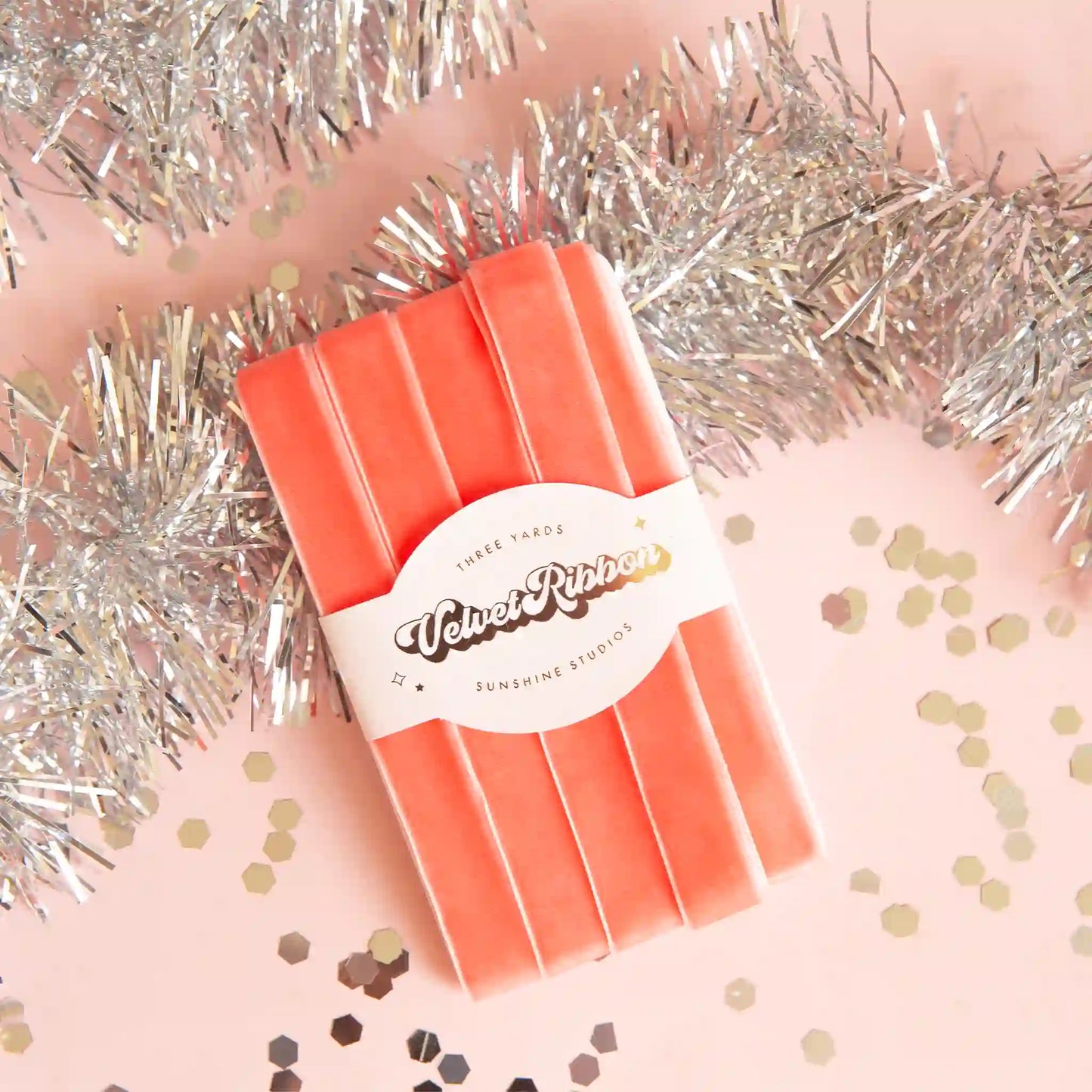 On a pink and tinsel background is a spool of peach velvet ribbon. 
