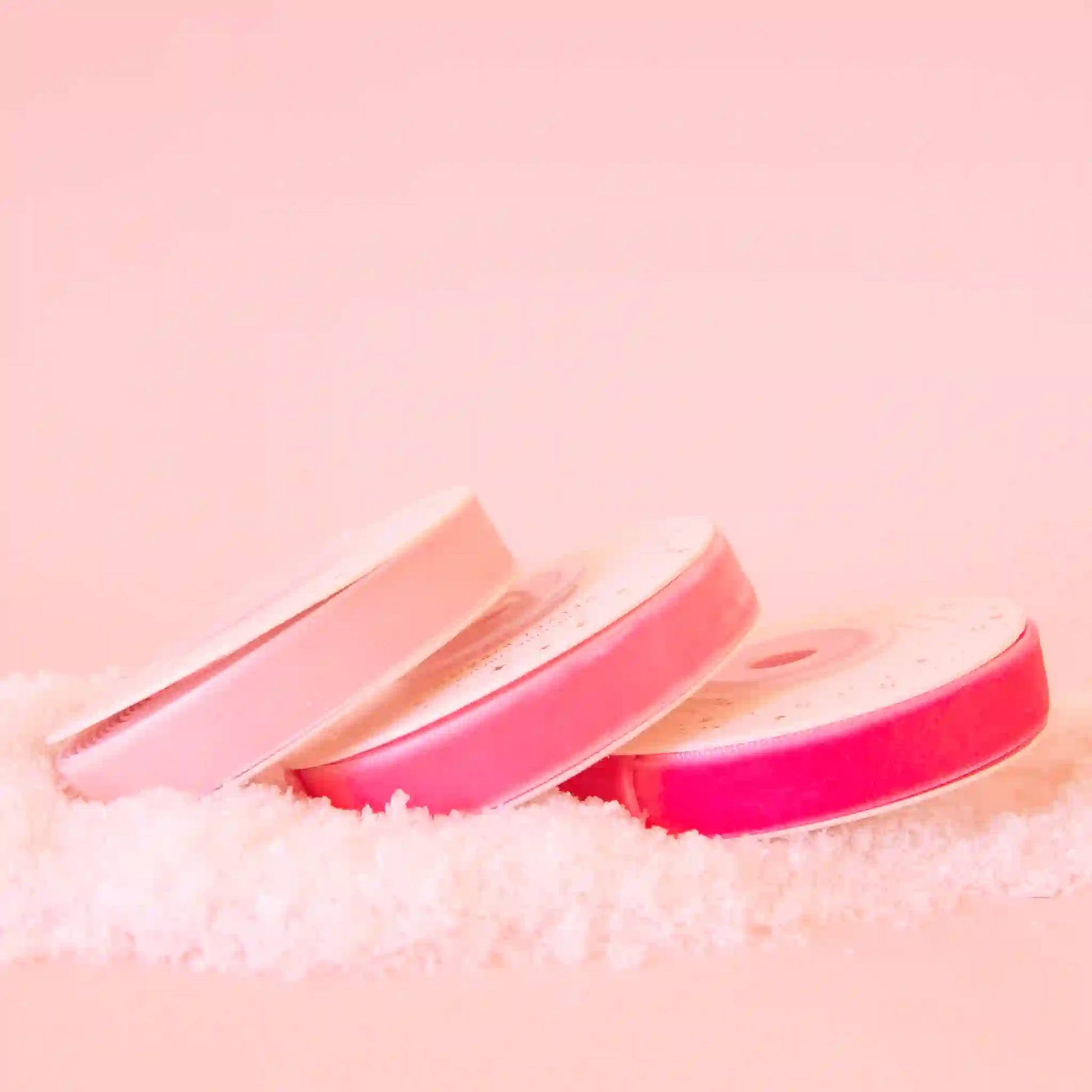 On a pink background is the three spools of velvet ribbon in three different shades of pink.