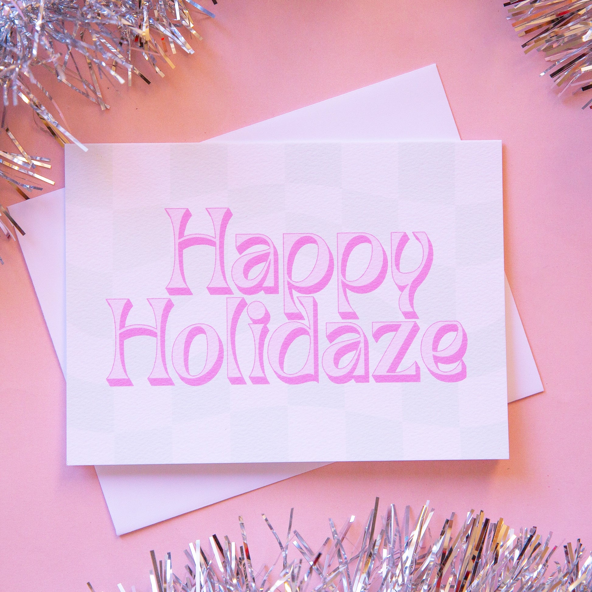 Pale mint and cream checkered card that reads 'Happy Holiday' in retro pink lettering with thin magenta shadow. The card is accompanied by a solid white envelope.