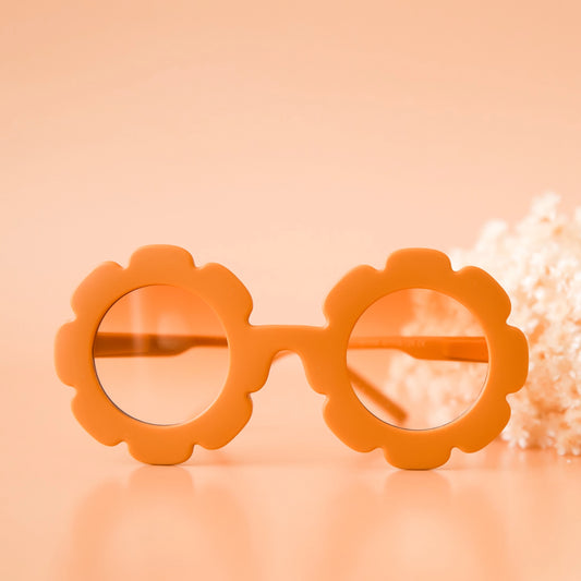 On a peachy background is a pair of orange, flower shaped sunglasses with a light orange lens.
