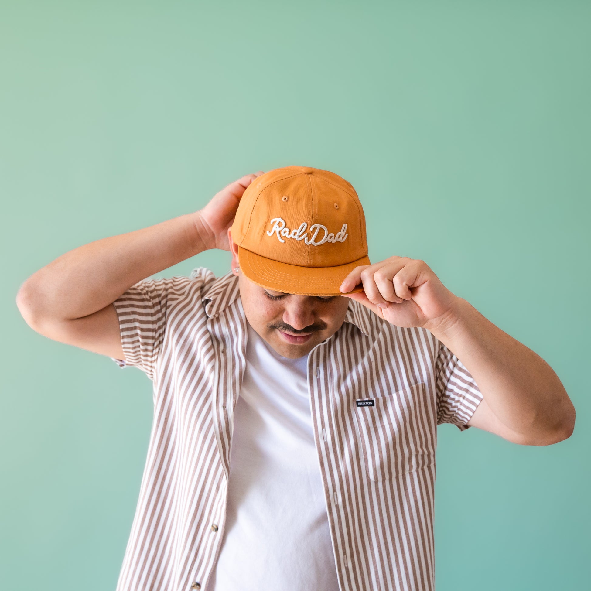 A flat brimmed burnt orange had with white embroidering that reads, "Rad Dad".