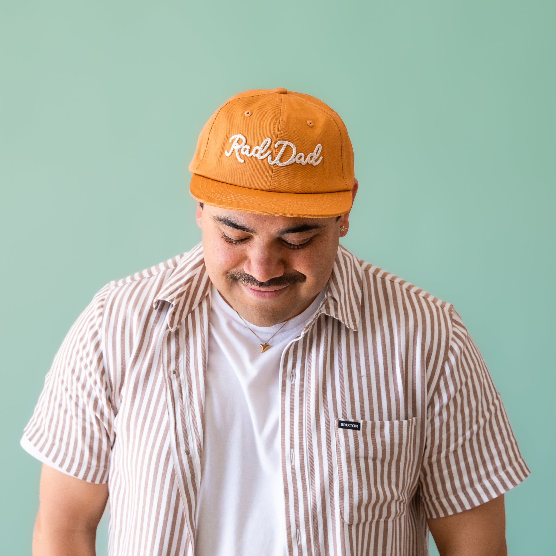 A flat brimmed burnt orange had with white embroidering that reads, "Rad Dad".