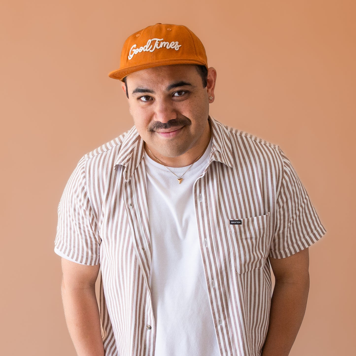 A burnt orange flat brim hat that reads, "Good Times" in ivory embroidered text.