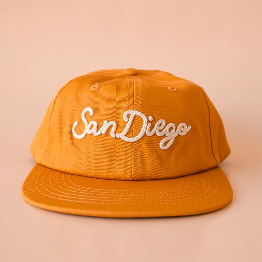 A burnt orange flat brim hat with ivory embroidered text that reads, "San Diego".