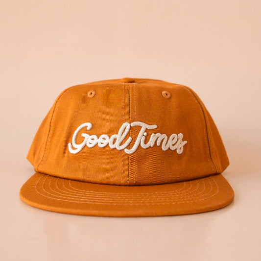 A burnt orange flat brim hat that reads, "Good Times" in ivory embroidered text.
