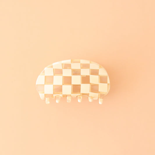 On a peachy background is an ivory and clear checker printed claw clip with a rounded edge.
