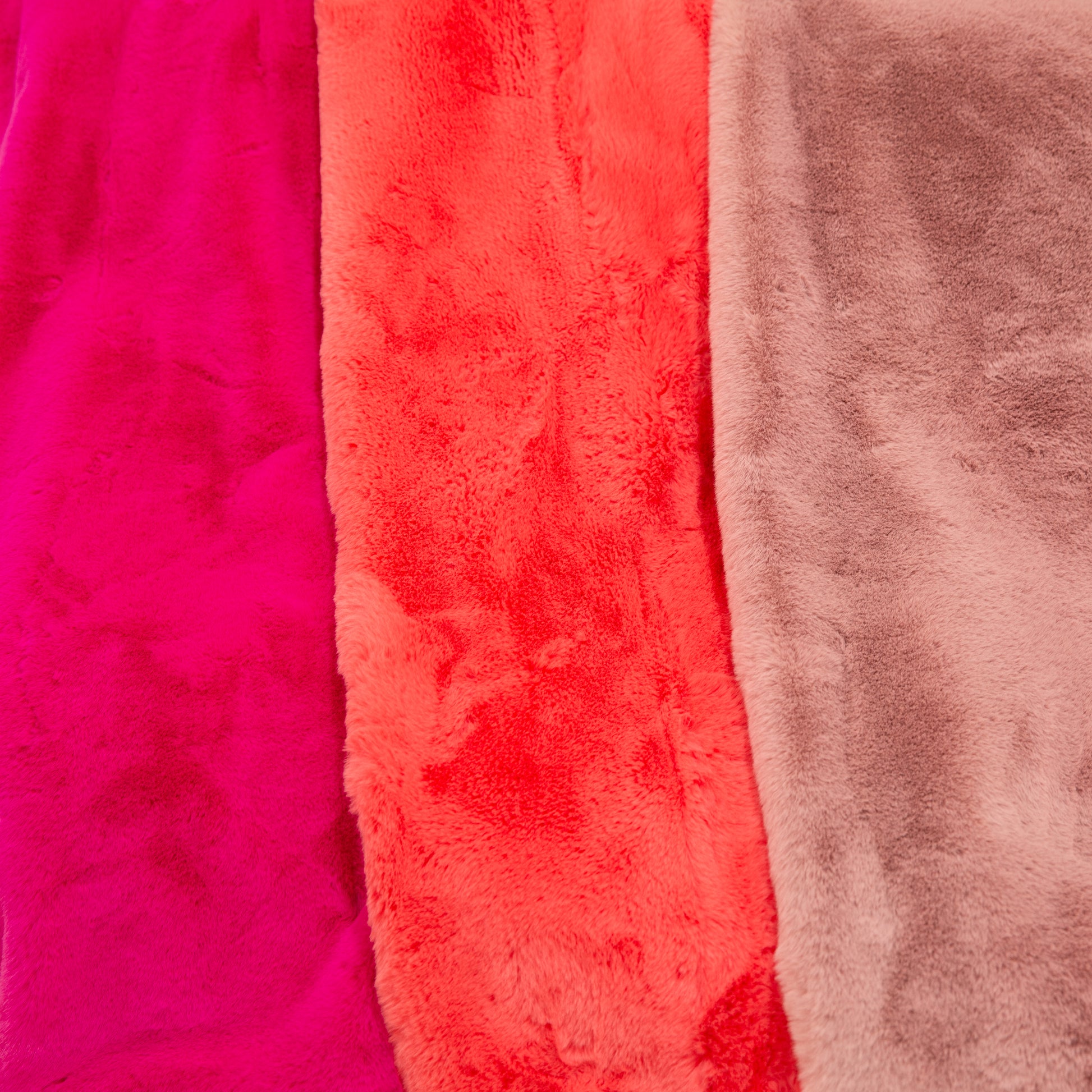 Three different shades of the luxe faux fur throw blankets next to one another. From left to right there is fuchsia, watermelon and dusty rose.